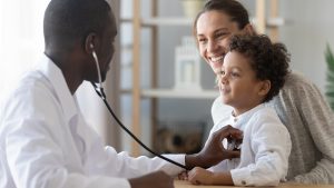 Doctor performing a child health checkup with a parent present in a medical office.